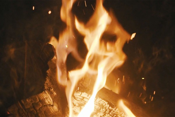 Bright flames dance over glowing embers in a cozy fire.